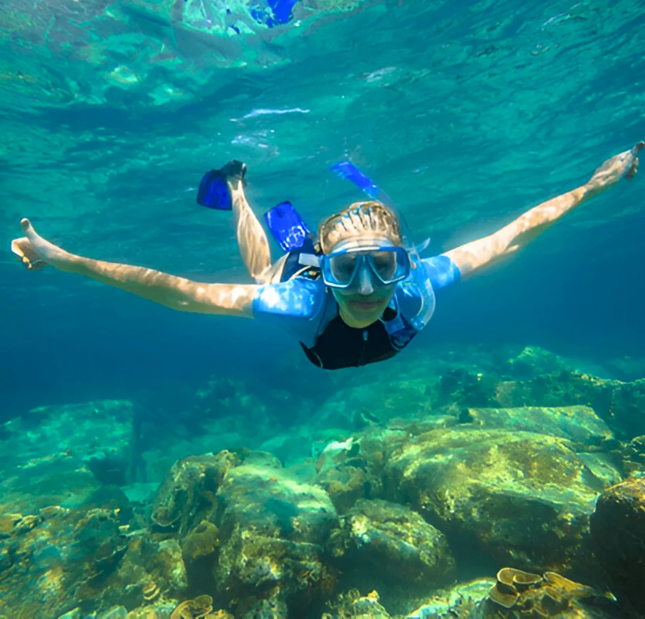 A woman in a blue shirt and snorkel explores the vibrant underwater world while snorkeling in the Andaman Sea.